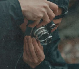 Close-up of a person holding and looking through a vintage-style camera, with hands adjusting the lens and body of the device