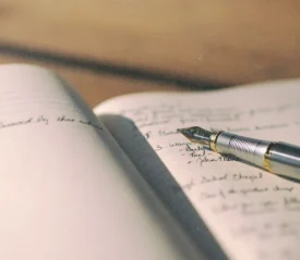 A fountain pen rests on the open pages of a notebook filled with handwritten notes, lit by warm natural light