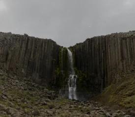 Tall waterfall cascading through a narrow gap between vertical basalt rock columns