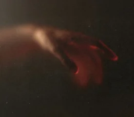 Softly lit hand reaching out in a dark, shadowy environment with a warm red glow along the fingers