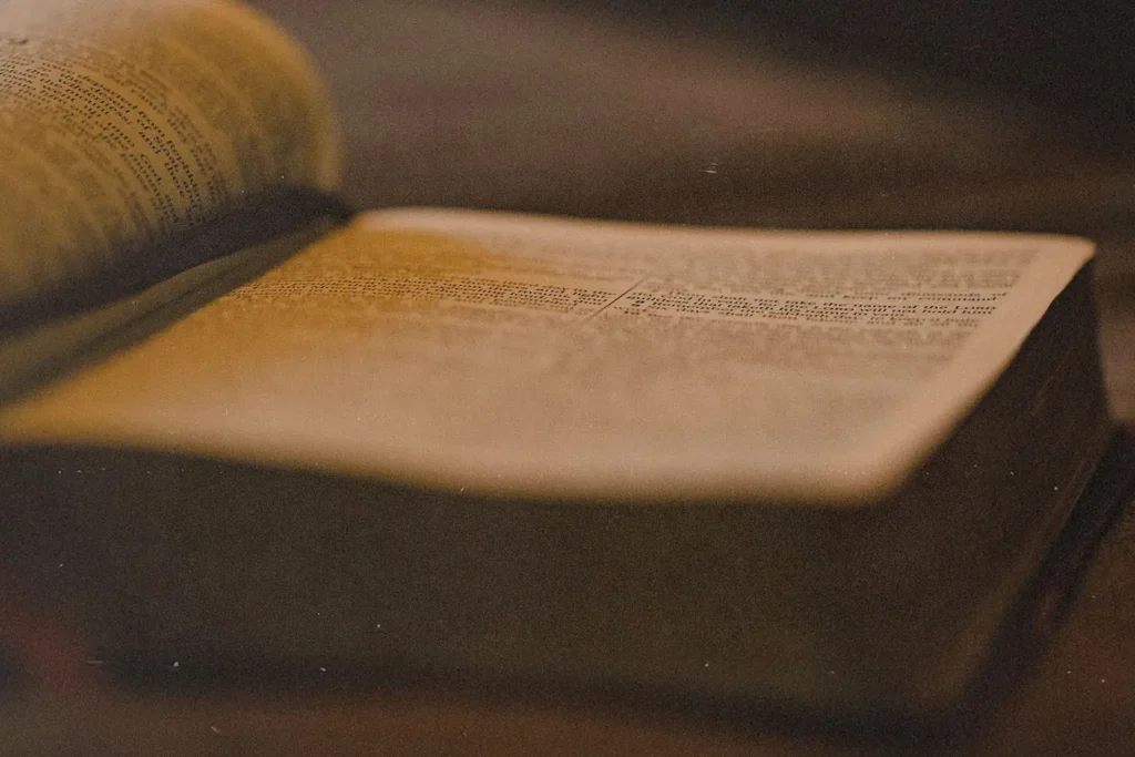 Close-up of an open Bible lying on a table, softly lit with warm, golden light highlighting the printed text