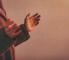 A person extends both hands outward in a gentle, open‑palmed gesture against a warm, softly lit background