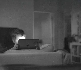 A child sits on a couch in a dim room, holding a tablet with soft light reflecting from the screen