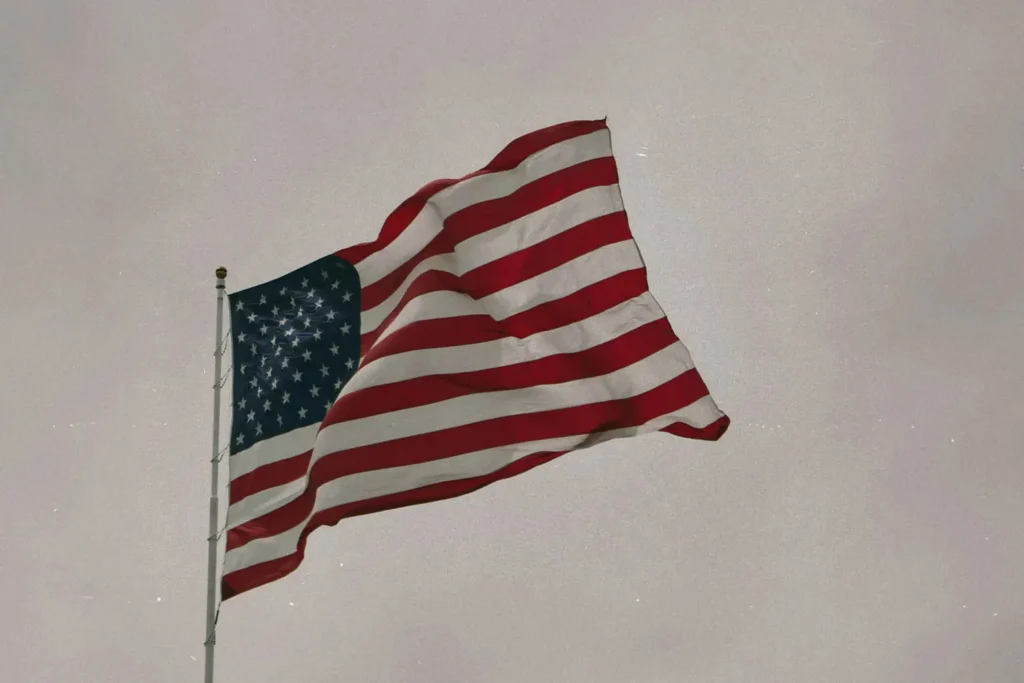 An American flag waves on a tall flagpole against a muted, overcast sky