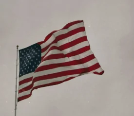 An American flag waves on a tall flagpole against a muted, overcast sky