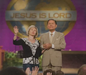 Kenneth and Gloria Copeland standing at the pulpit in prayer