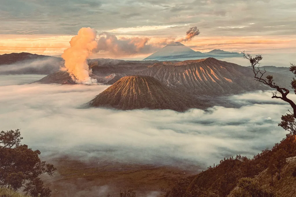 Dramatic volcanic landscape with steaming craters rising above a sea of clouds at sunrise