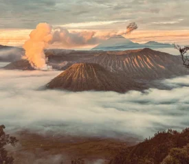 Dramatic volcanic landscape with steaming craters rising above a sea of clouds at sunrise