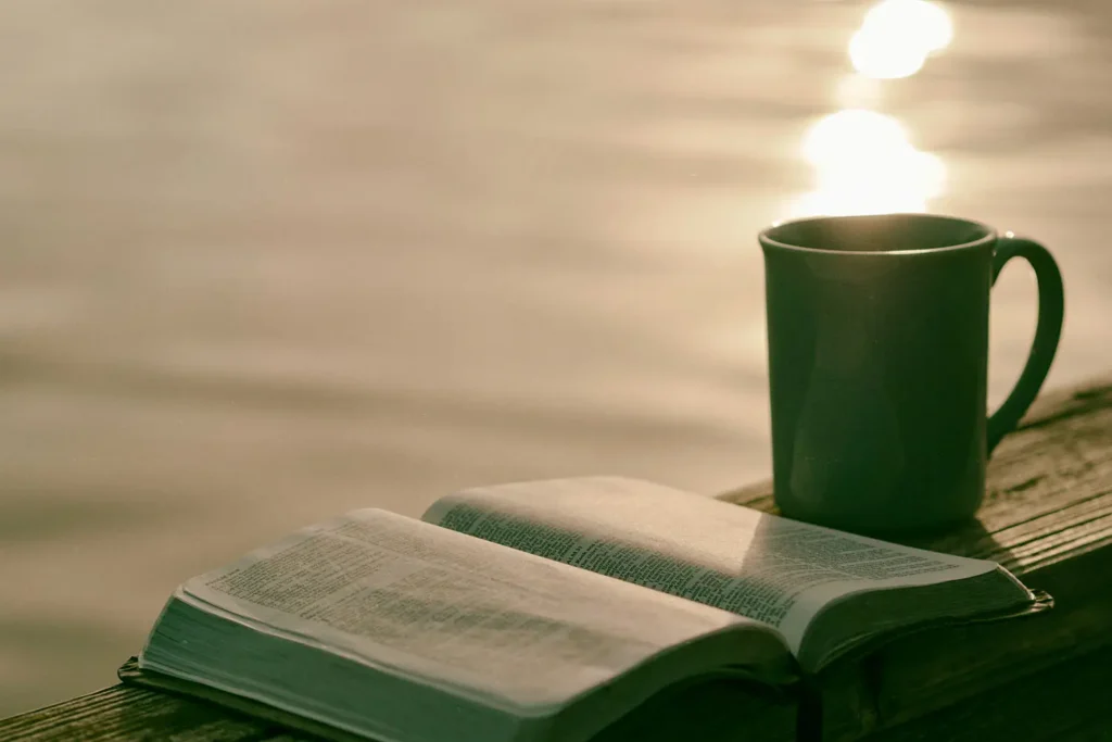 Open Bible and coffee cup resting on ledge overlooking a body of water