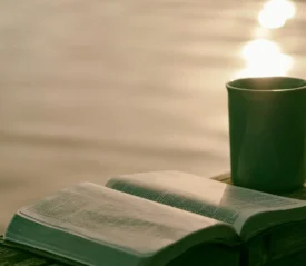 Open Bible and coffee cup resting on ledge overlooking a body of water