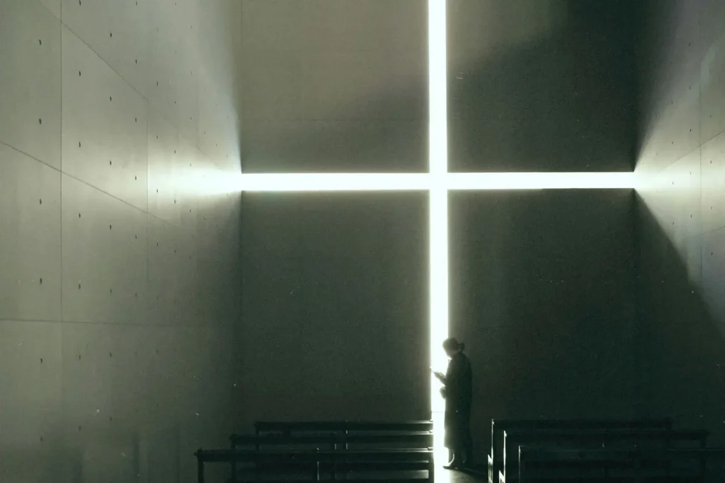 Person standing in between pews and a bright light that forms a tall thin cross
