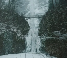 Icy waterfall framed by rocky cliffs and a stone bridge overhead on a snowy day
