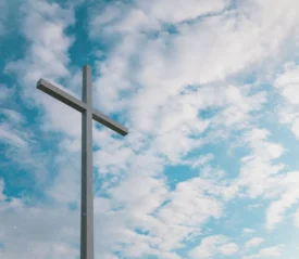 Large metal cross standing against a bright sky filled with scattered white clouds