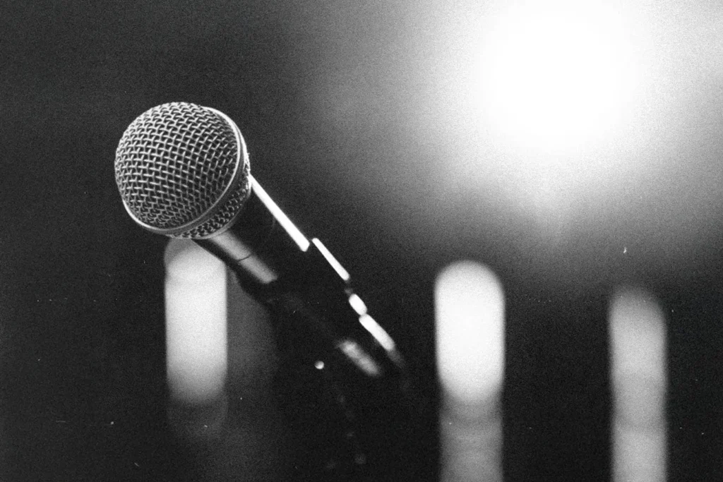 Close-up of a microphone on a stand with bright stage lights glowing in the background
