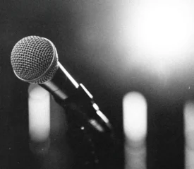 Close-up of a microphone on a stand with bright stage lights glowing in the background