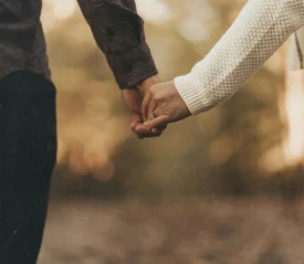 Two people holding hands outdoors with warm, soft sunlight in the background