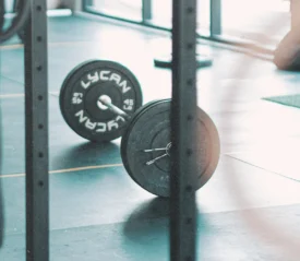 Barbell loaded with weight plates resting on a gym floor in a bright workout space