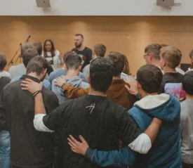 Group of people standing in a circle with arms linked and praying