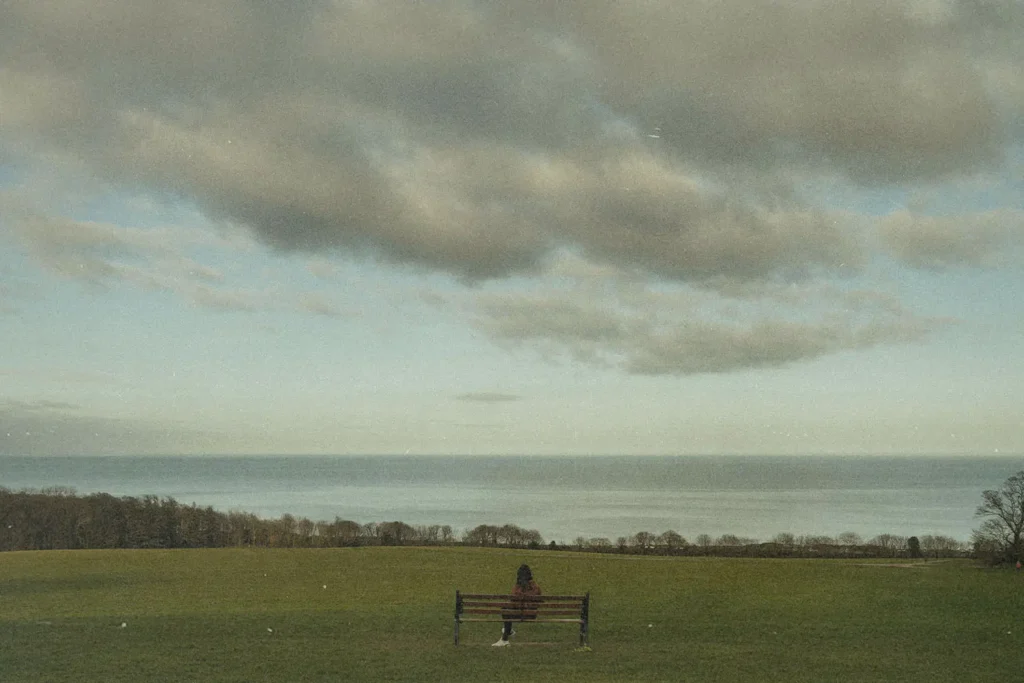 Person sitting on a bench in the middle of grassy field overlooking ocean view