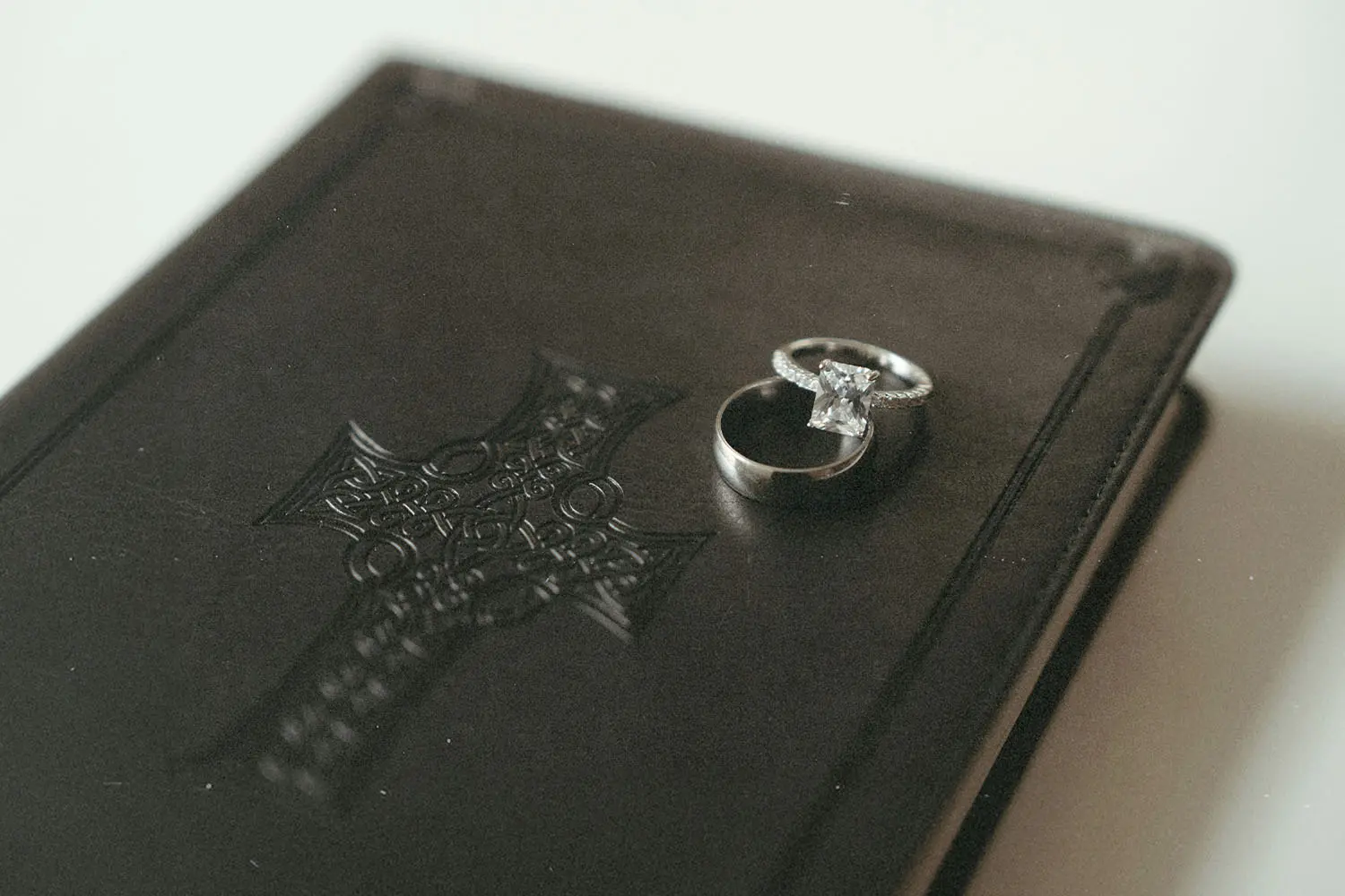 Wedding rings resting on top of a closed leather Bible embossed with a decorative cross