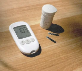 Blood glucose meter reading “103” with test strips and a container on a wooden table