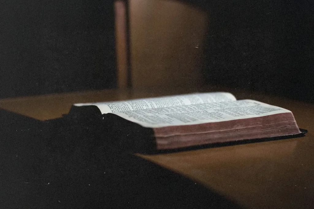 Open Bible resting on a wooden surface in soft, low light