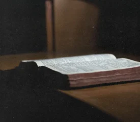 Open Bible resting on a wooden surface in soft, low light