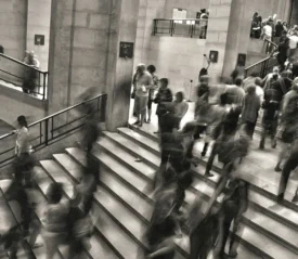 black and white photo of people walking up and down stairs in a busy scene