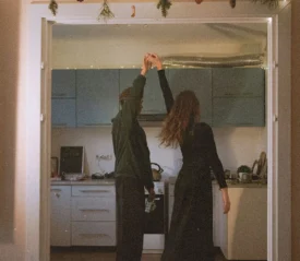 Two people dance together in a warmly lit kitchen, holding hands as they spin between the doorway and the counter