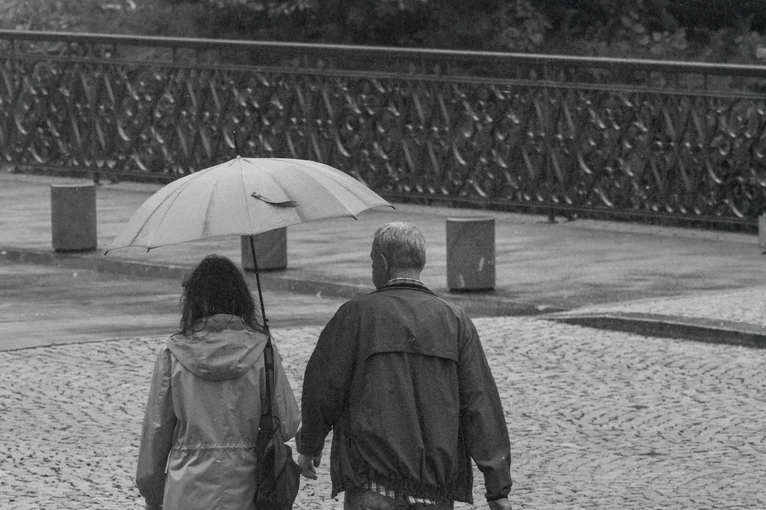 man and woman walking with an umbrella in a park like setting