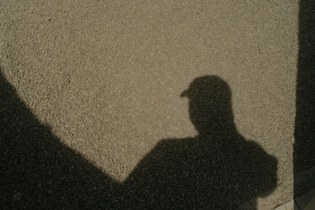 shadow of a person wearing a hat on gravel