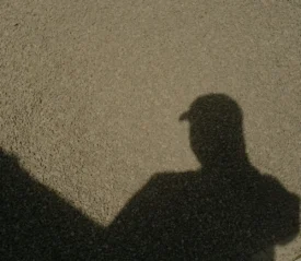 shadow of a person wearing a hat on gravel
