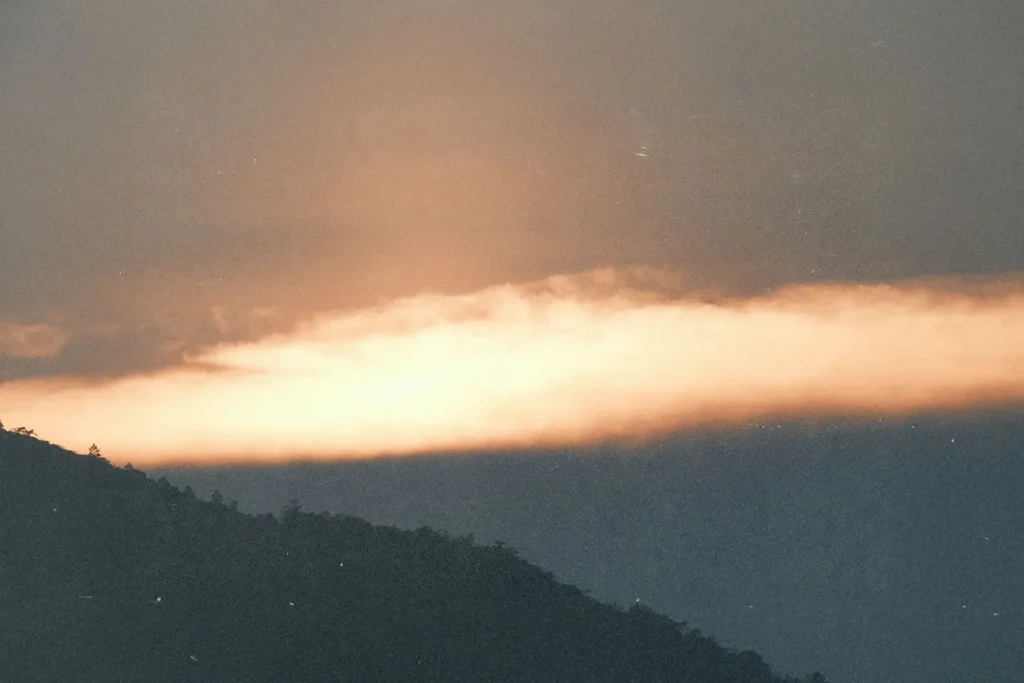 A glowing band of orange light spreads across the horizon at sunset, illuminating the sky above the dark silhouette of a mountain ridge