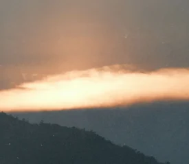 A glowing band of orange light spreads across the horizon at sunset, illuminating the sky above the dark silhouette of a mountain ridge