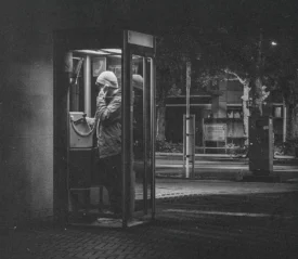 Person standing in a lit phone booth at night on a quiet street