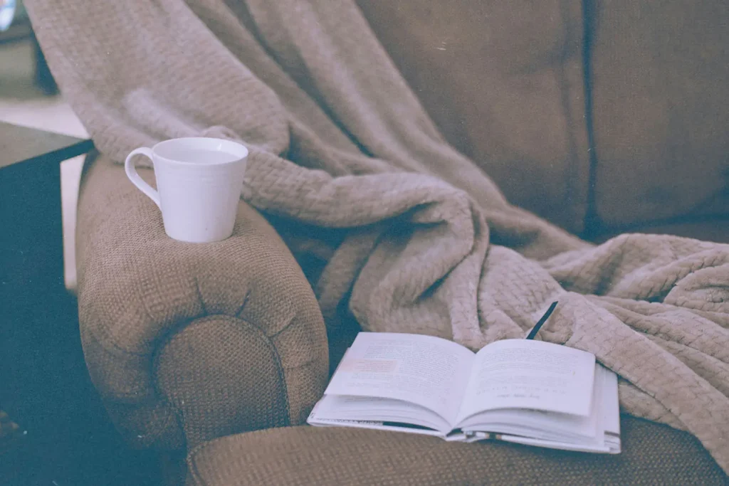 book open on a chair with a mug and a blanket