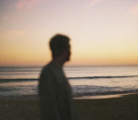 Silhouetted figure standing on the beach at sunset with gentle waves rolling onto the shore