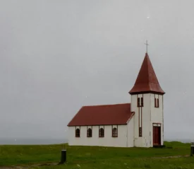 older white church with red roof in the middle of a field