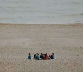Friends gathered in a circle on a sandy beach near gentle ocean waves