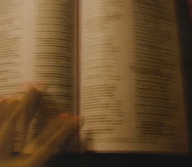 A blurred close‑up of an open Bible with a hand gliding across the page, softly lit in warm tones