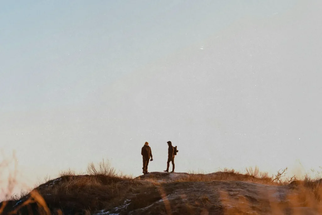 Hikers silhouetted against an open sky while standing on a ridge with dry grass