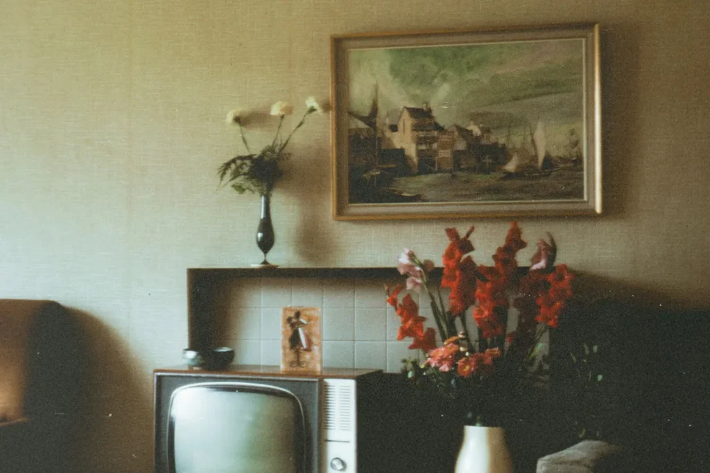 Vintage living room with an old television, floral arrangements, and a framed painting hanging above a tiled fireplace