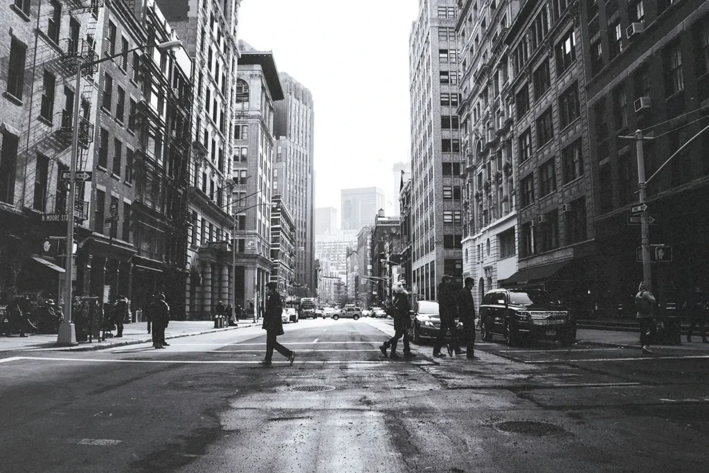 black and white photo of people walking across a crosswalk in the city