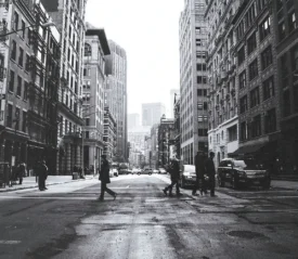 black and white photo of people walking across a crosswalk in the city