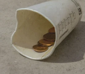 cup laying on ground with loose coins inside