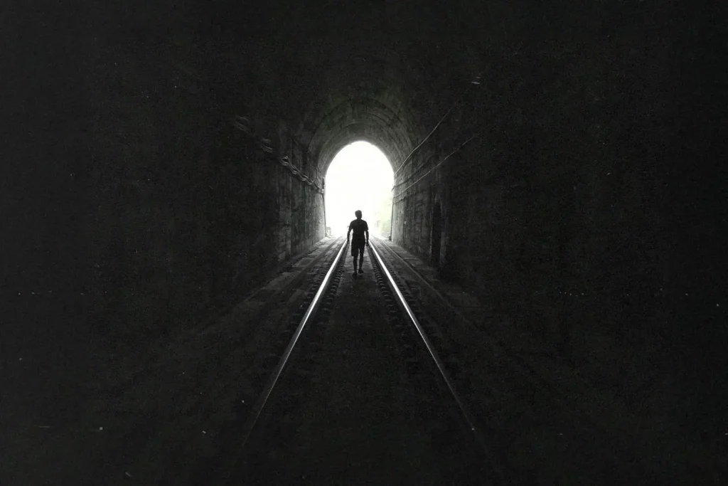 Man walking on train tracks in a tunnel towards light
