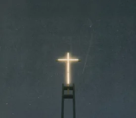 A glowing cross sits atop a tall structure against a dark, starless night sky