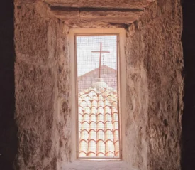 looking out of a wired window at a cross on top a building
