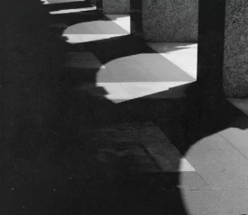 Strong contrast of light and shadow cast by a row of stone columns onto a tiled walkway