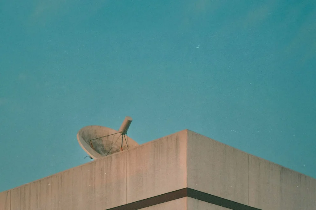 Satellite dish mounted on the corner of a concrete building against a clear blue sky